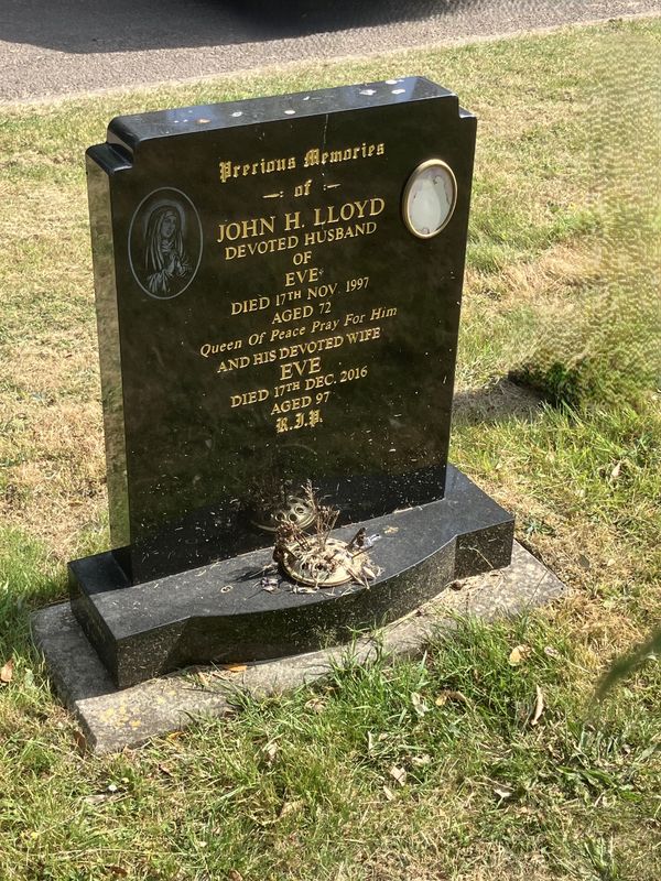 Upright granite headstone with withered flowers before a Calon visit